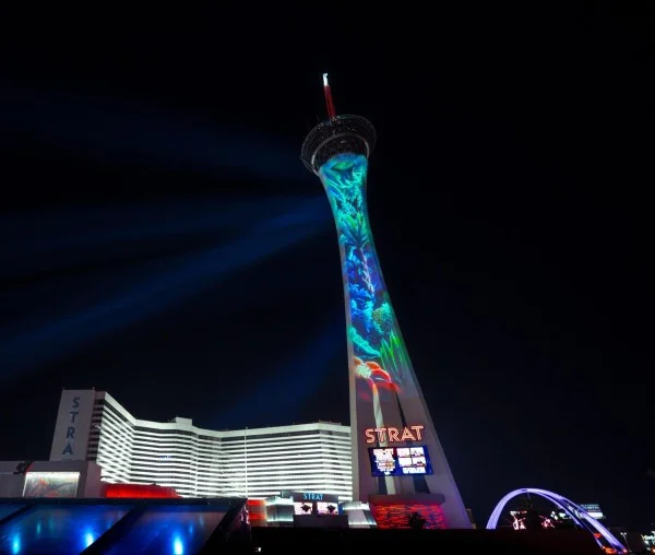 The Stratosphere Casino Tower illuminated at night, featuring vibrant projections and colorful lights against a dark sky